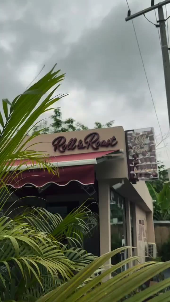 Roll & Roast café exterior with its sign, burgundy awning and greenery.